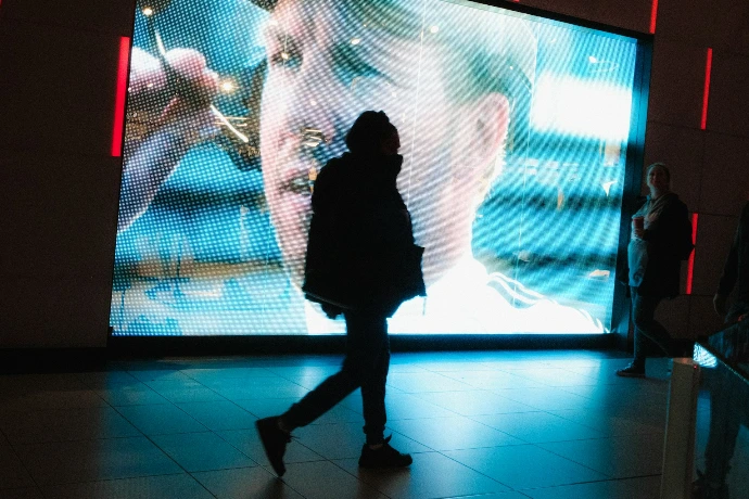 Person walks past large screen showing a man's face.